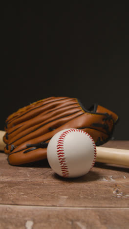 Vertical-Video-Close-Up-Studio-Baseball-Still-Life-With-Wooden-Bat-And-Ball-In-Catchers-Mitt-On-Wooden-Floor